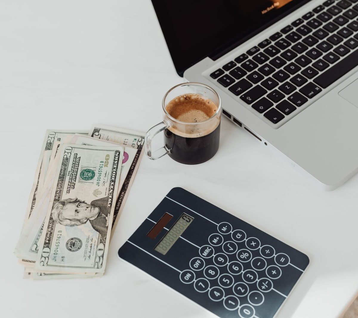 Banknotes, a calculator, a coffee and a laptop on a white desk, illustrating YouTube creator earnings