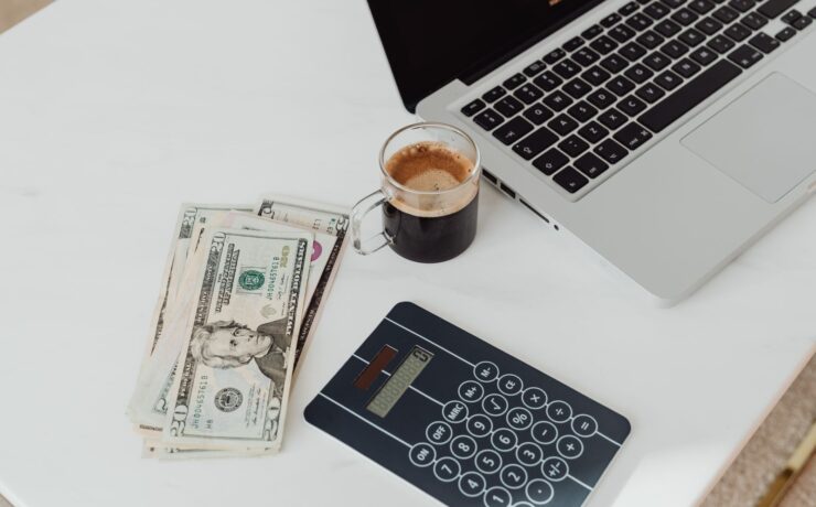 Banknotes, a calculator, a coffee and a laptop on a white desk, illustrating YouTube creator earnings