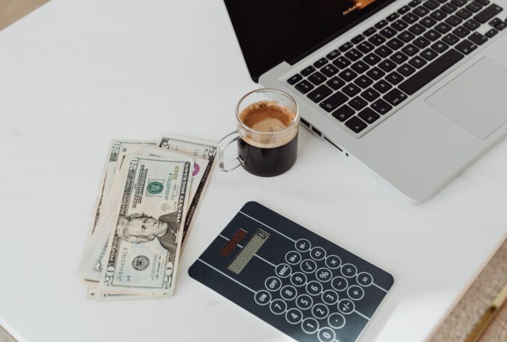 Banknotes, a calculator, a coffee and a laptop on a white desk, illustrating YouTube creator earnings