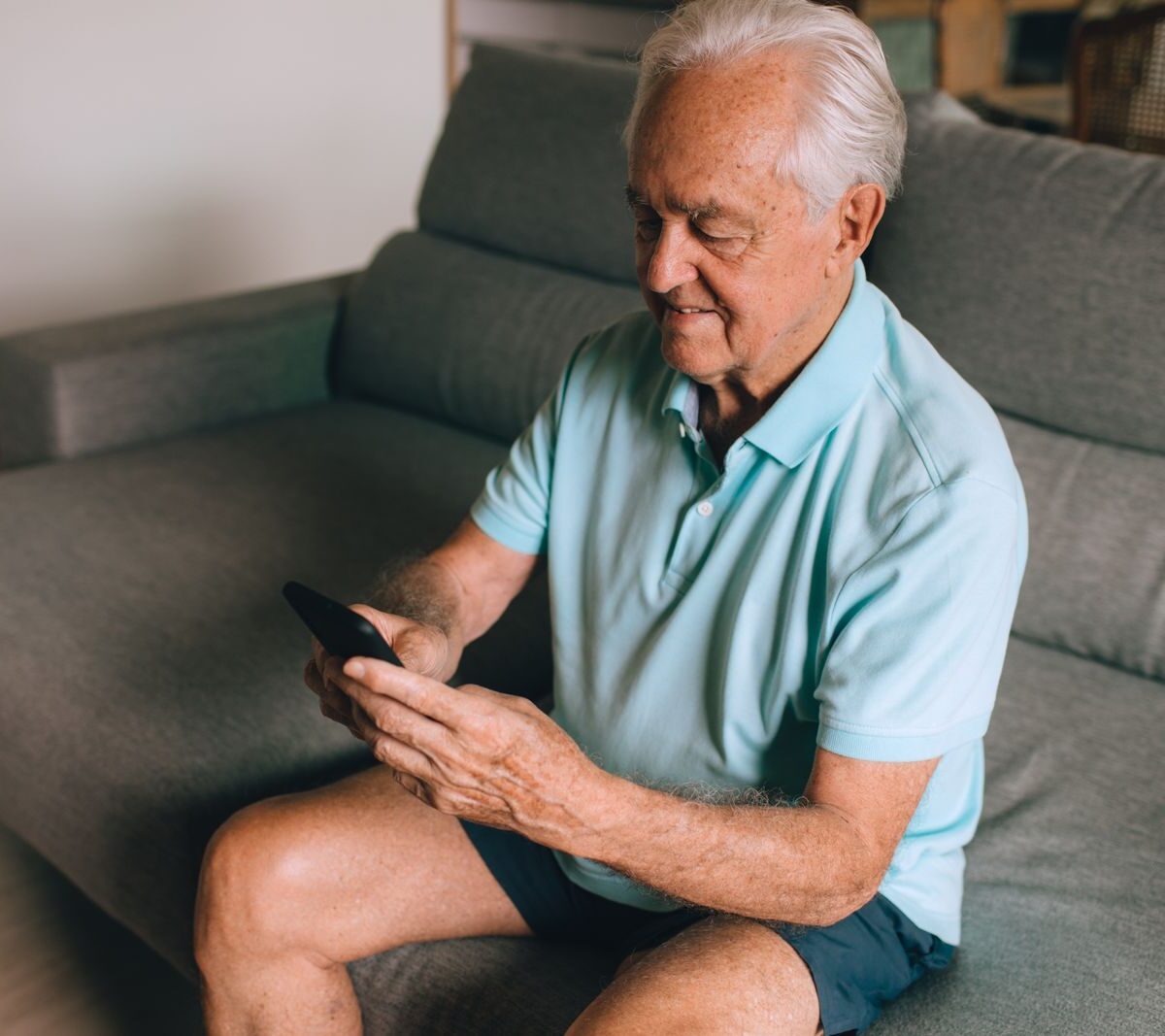 Man sitting on a grey sofa scrolling through recommended videos on his smartphone